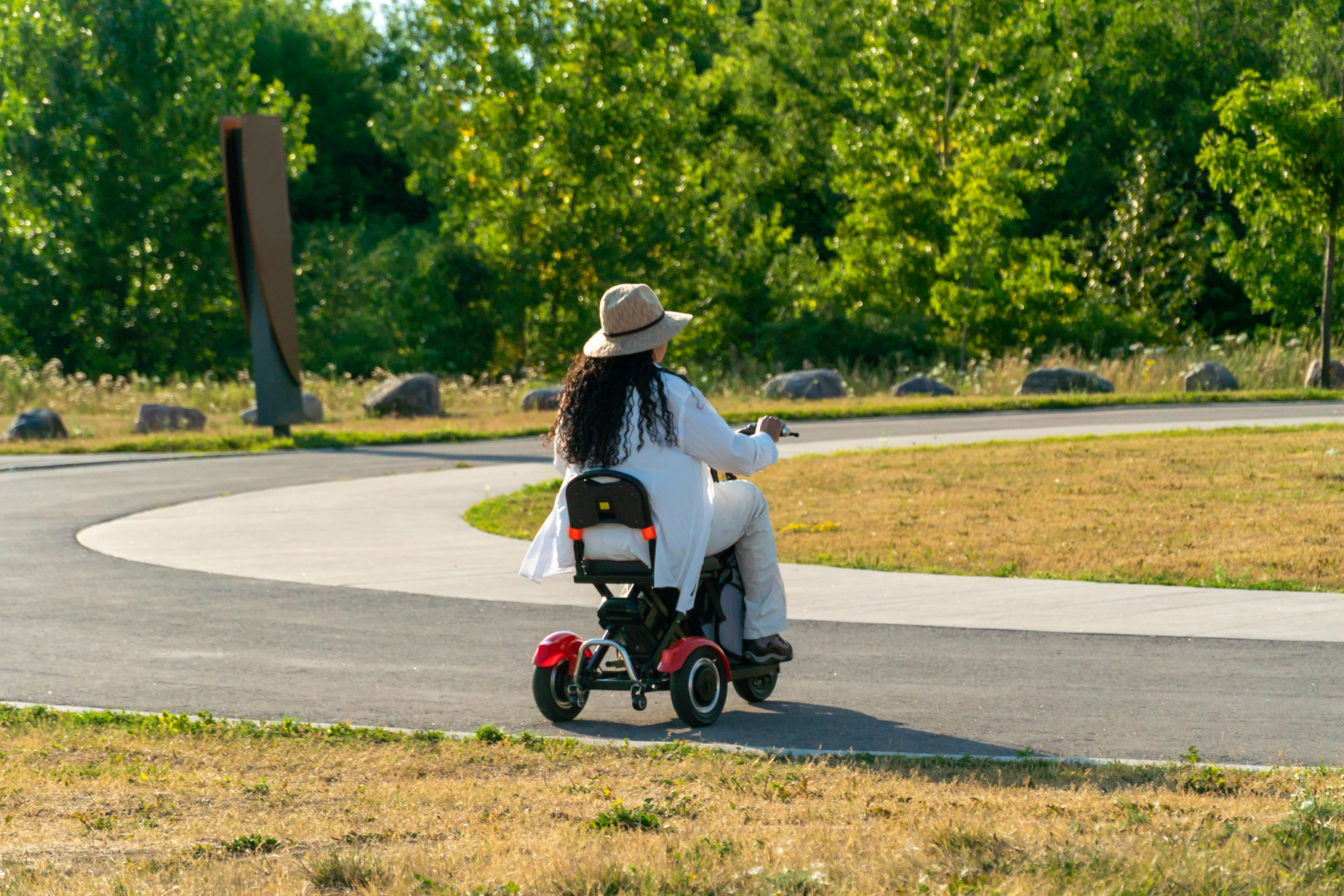 Woman with mobility issues in an electric scooter wheelchair driving around summer park in the evening. Mobility electric vehicle for independence and accessibility.